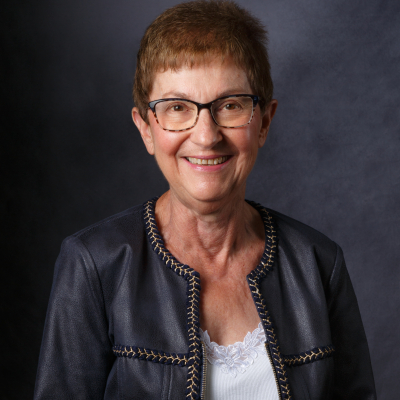 Professional photo of a person with a black leather jacket on. She is smiling at the camera and her body is turned towards the left.