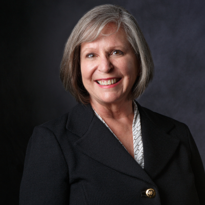 Professional photo of a person with a black blazer on. She is smiling at the camera and her body is turned towards her left.