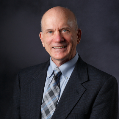 Professional photo of a person with a suit, dress shirt, and tie on. He is smiling at the camera and his body is turned towards his right.