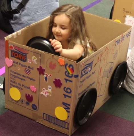 Child sitting in cardboard car